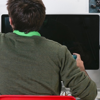 Man sitting at a computer while writing on a whiteboard behind the computer