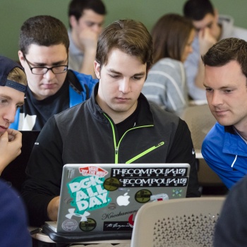 group of students, gathered around a laptop
