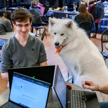 a white fluffy dog sits with three students studying