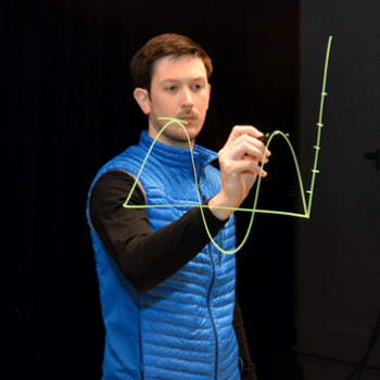 instructor writes on a clear glass board with an erasable marker