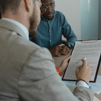 Man Holds a clipboard and pen while another person sits at a table