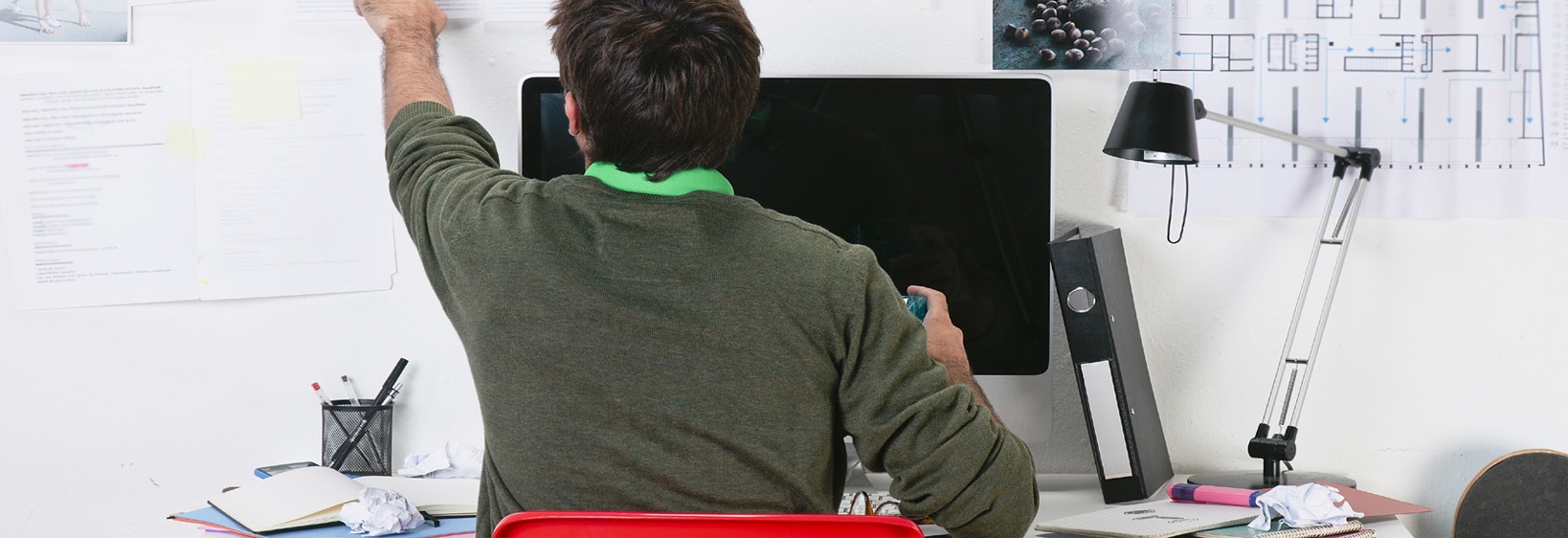 Man sitting at a computer while writing on a whiteboard behind the computer