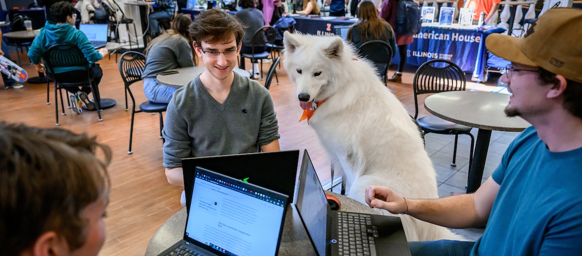 three students sitting with white fluffy dog