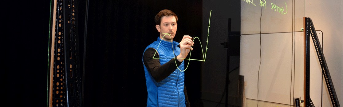 instructor writes on a clear glass board with an erasable marker